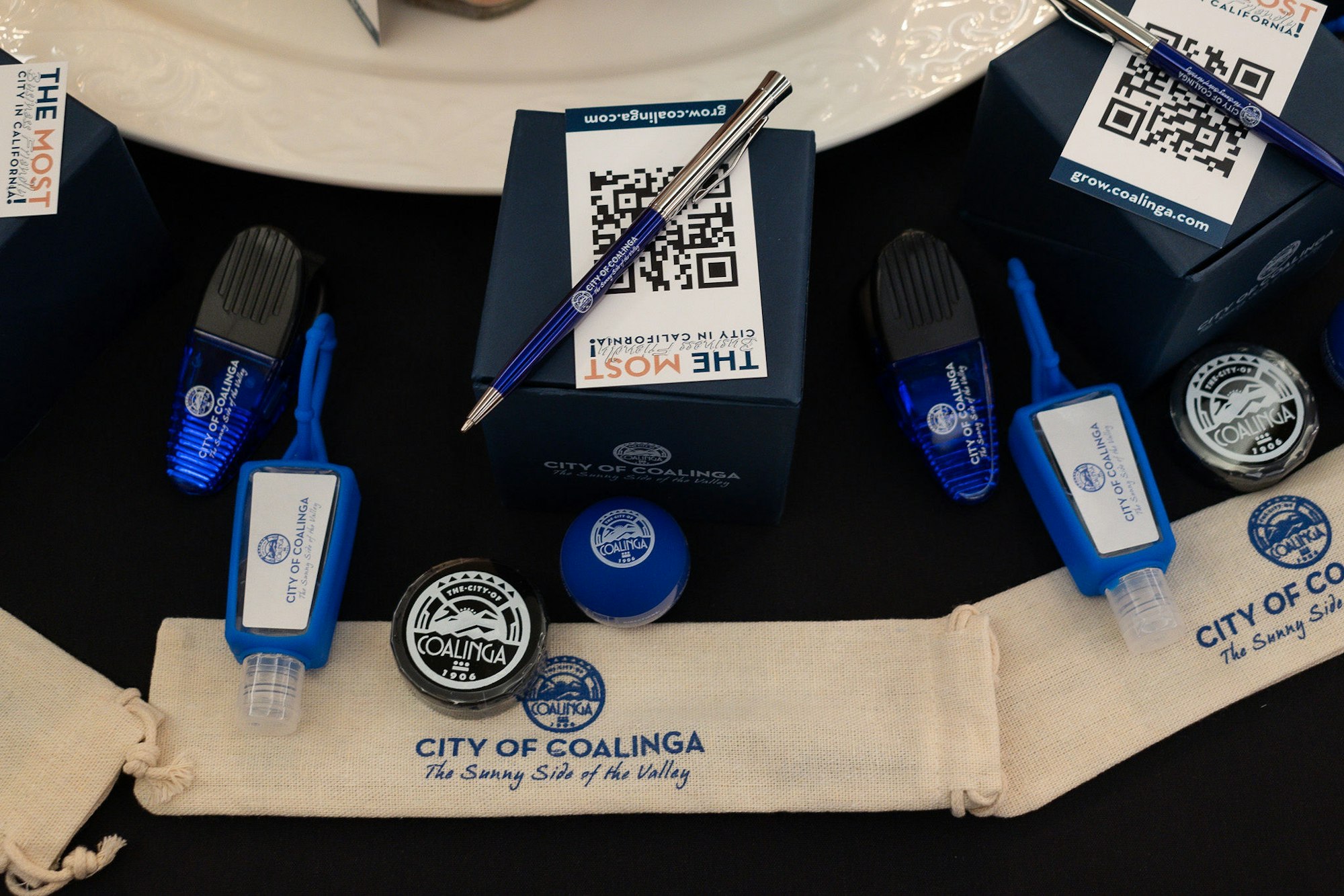 Promotional items for City of Coalinga, California including pens, sanitizers, and a chip clip, with QR code and slogan.