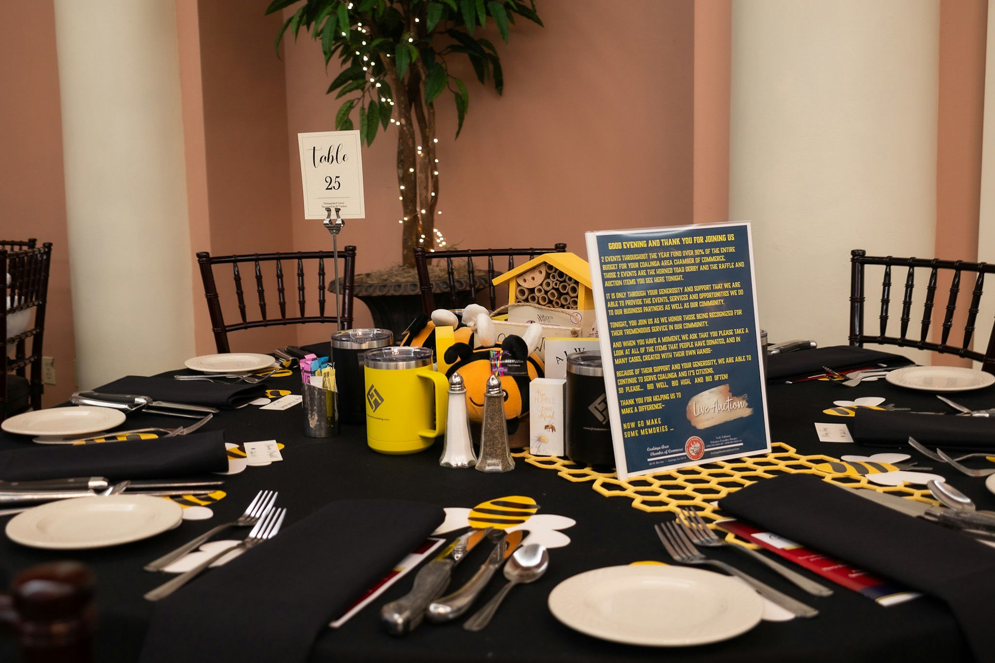 A banquet table set for an event with a black and yellow theme, numbered "Table 25" with a thank-you sign.