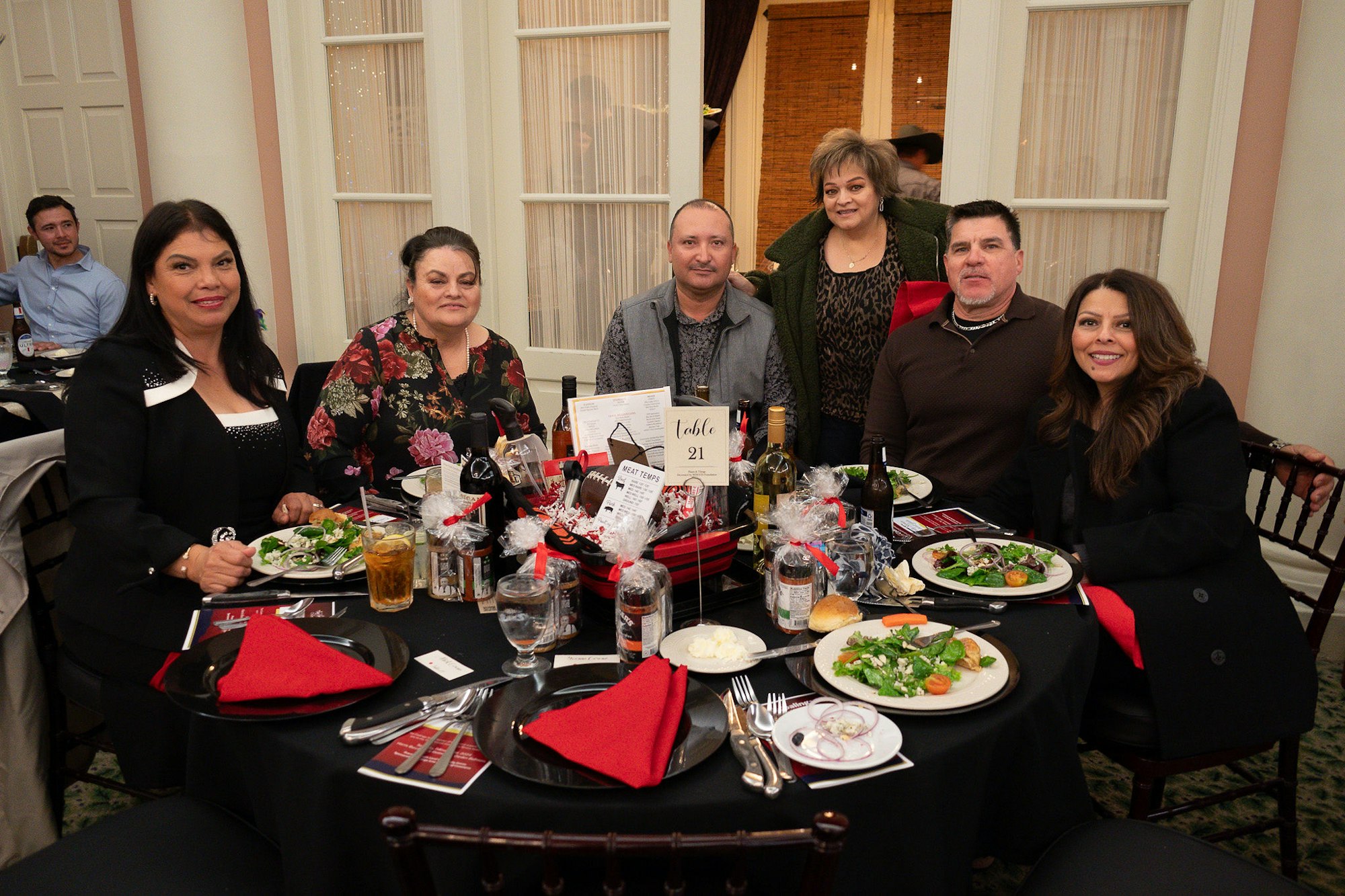 Group of people at a dinner event, sitting around a table with food and drinks, smiling for the camera.