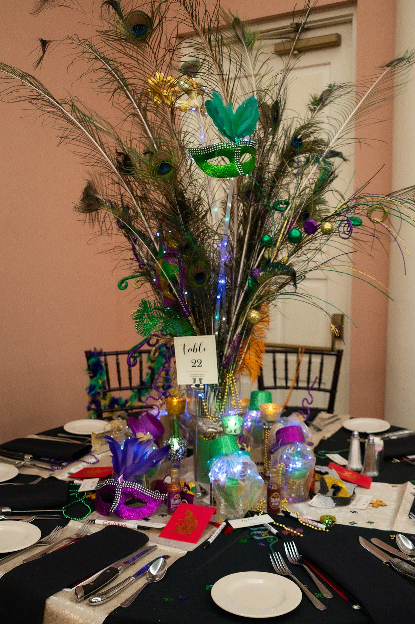 A festively decorated table with Mardi Gras theme, featuring masks, beads, and peacock feathers centerpiece. #MardiGrasDecor