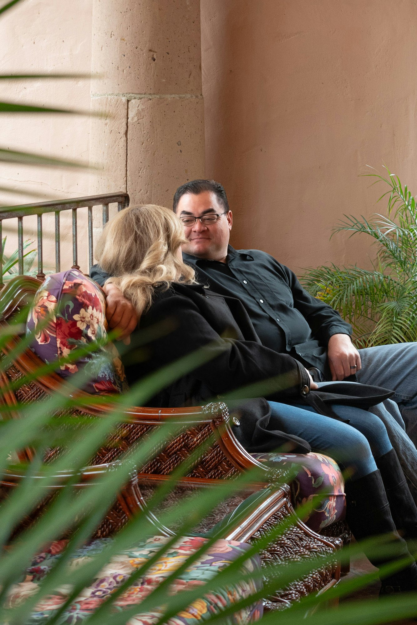 A couple seated on a bench, smiling, partially obscured by foliage.