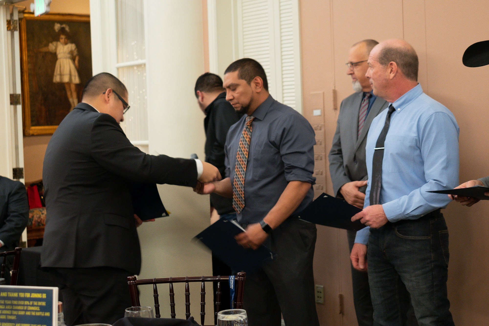 Men exchanging handshakes and documents in a formal ceremony indoors.