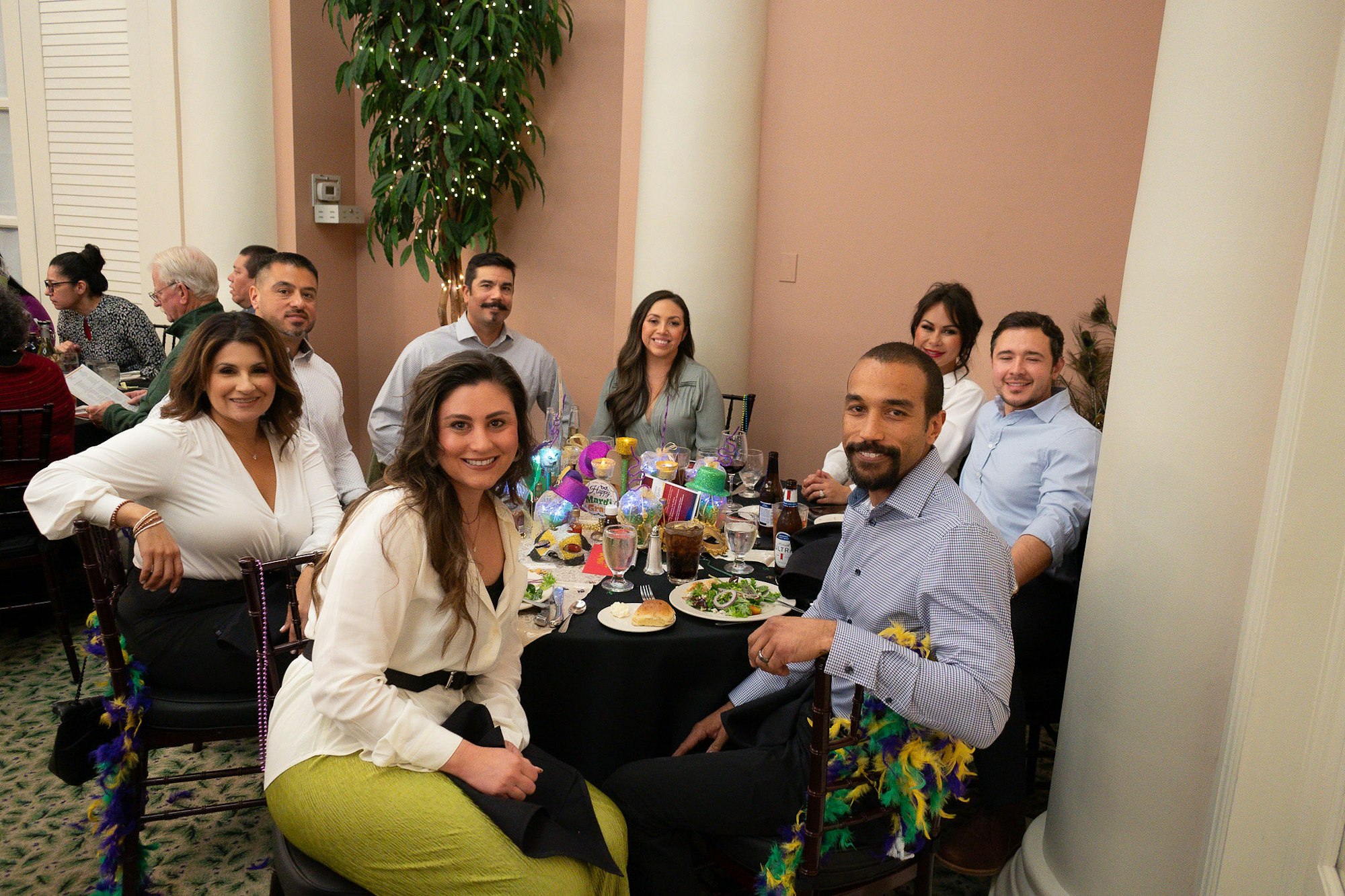 Group of people at a festively decorated table, smiling, with food and drinks, in a social gathering.