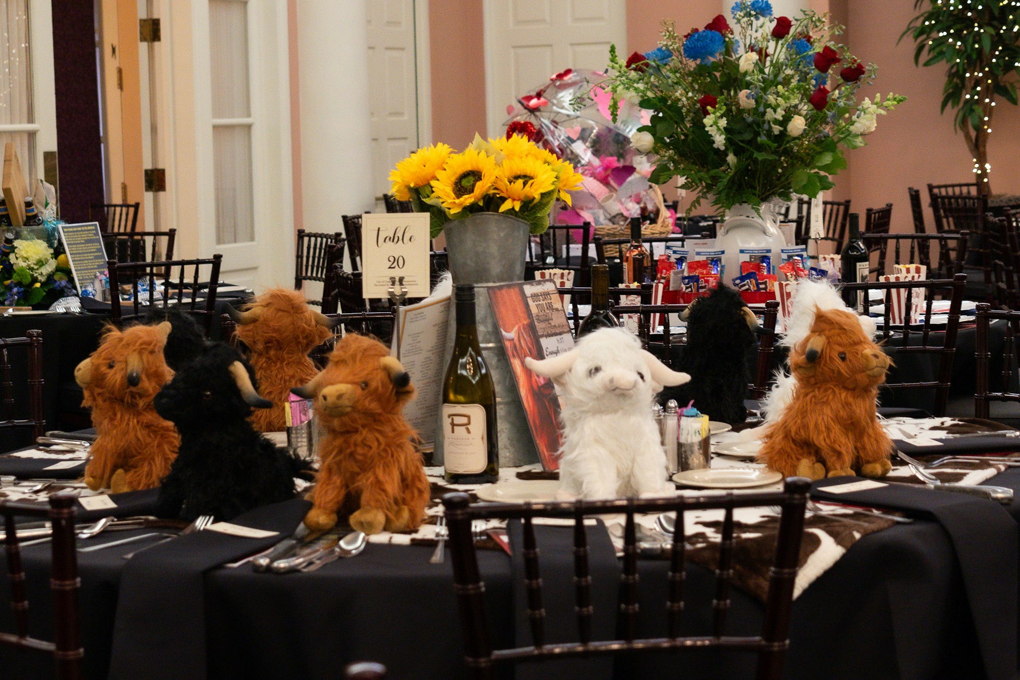 Puppet llamas at a decorated banquet table with sunflowers, a wine bottle, and dinner settings.