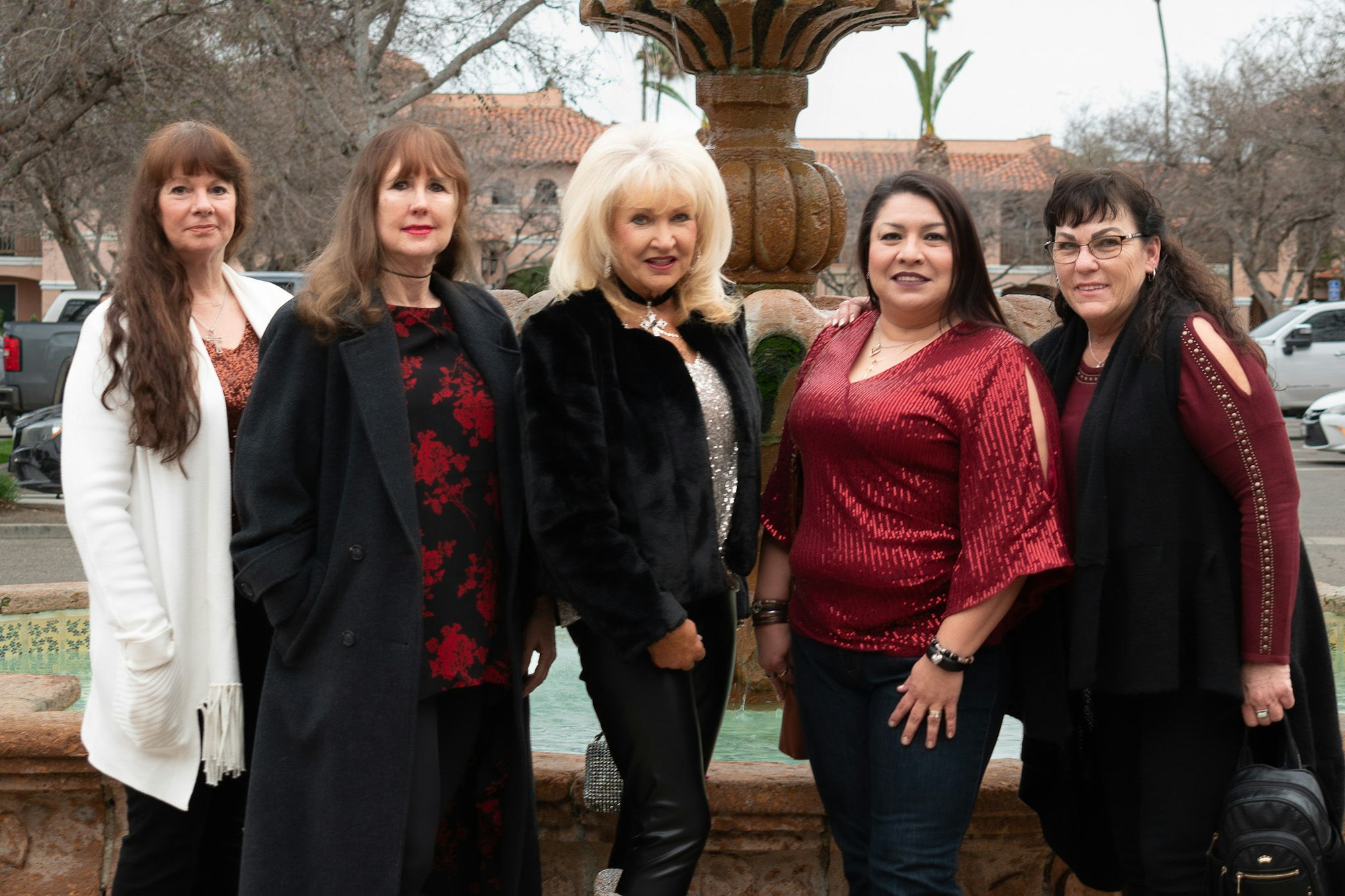Five women posing in front of a fountain, dressed in winter attire.