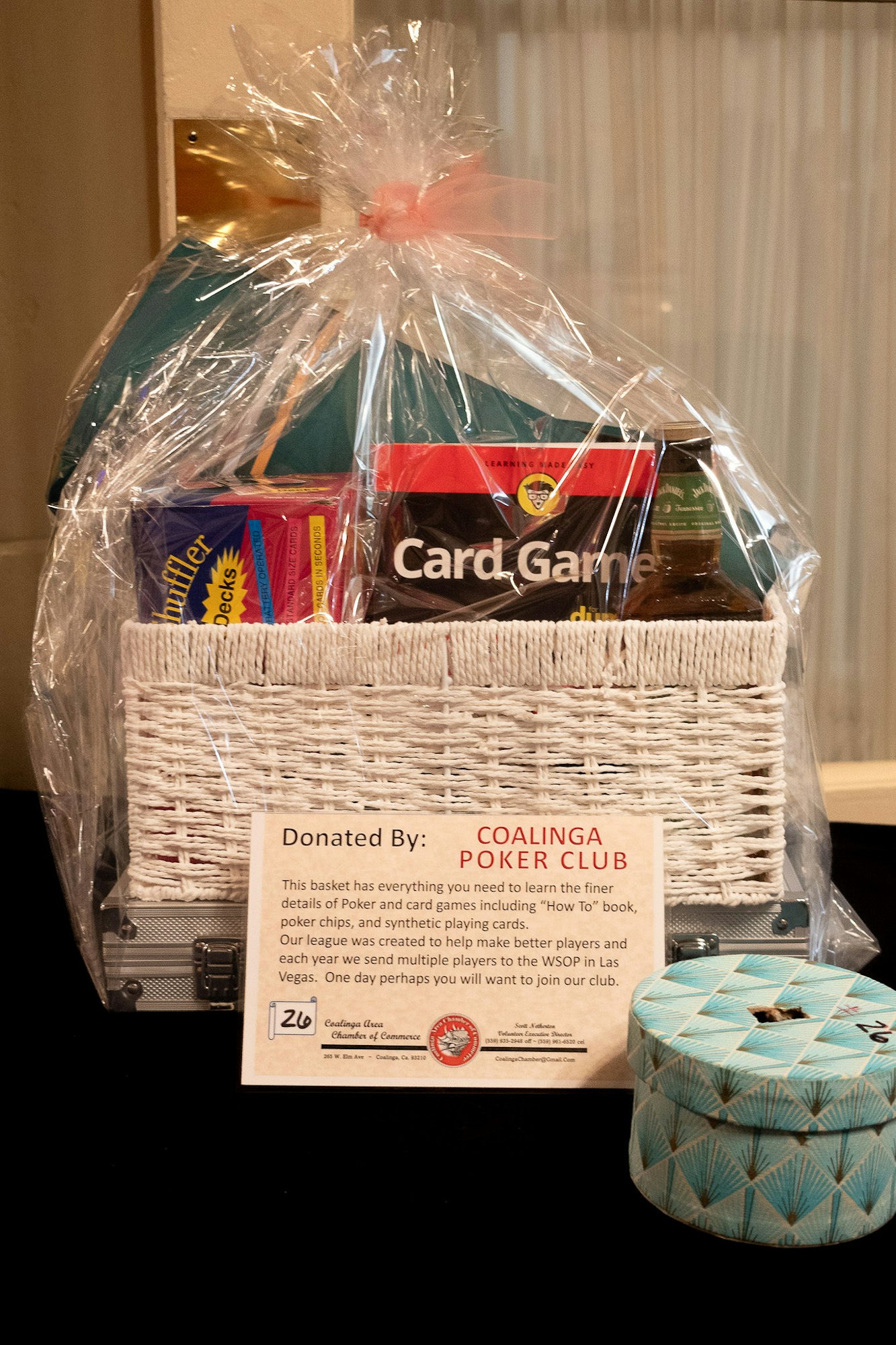 A gift basket with poker guides, chips, and cards, wrapped in plastic, with a "Donated By: COALINGA POKER CLUB" sign.