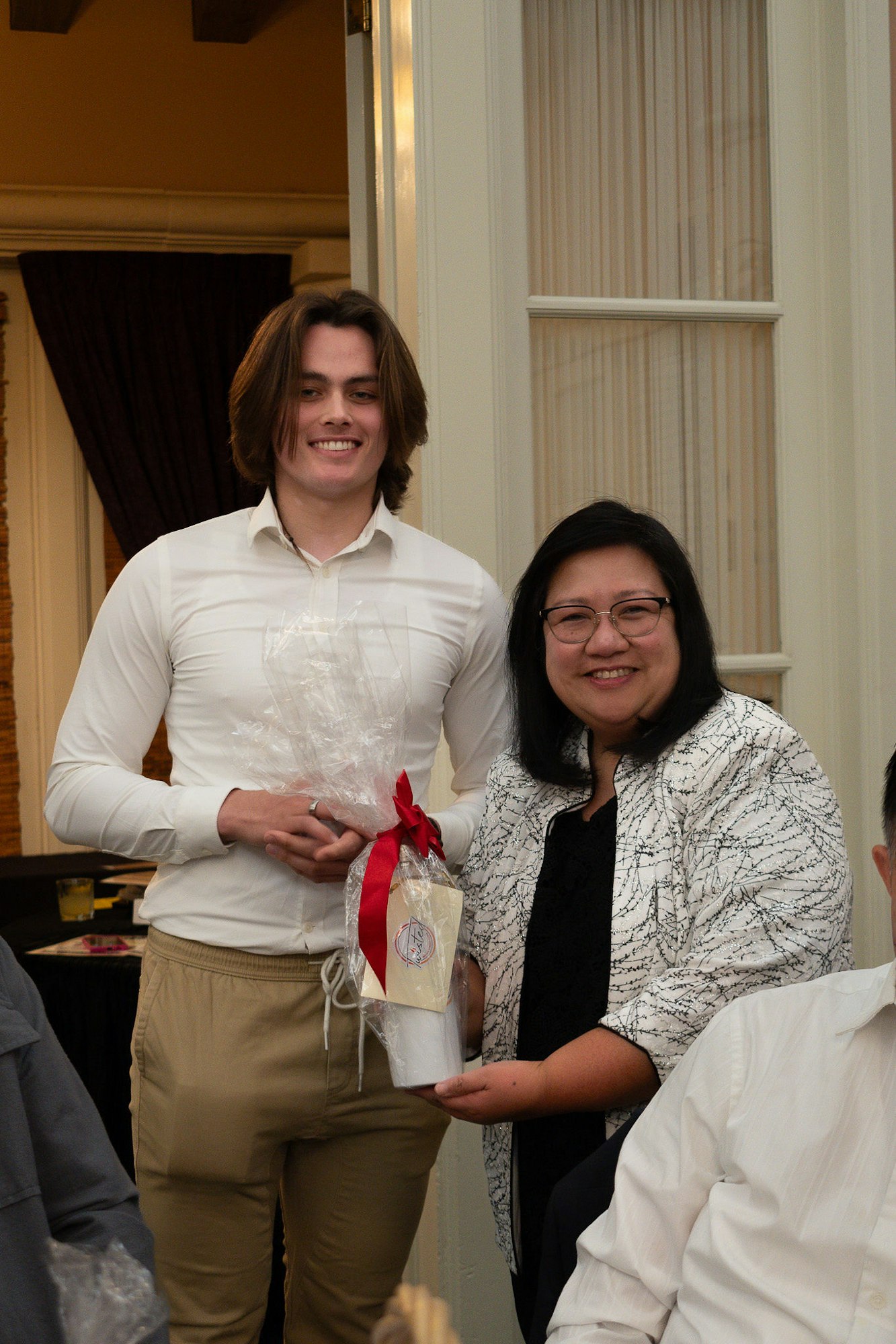 A man and a woman smiling, holding a gift with a red ribbon.