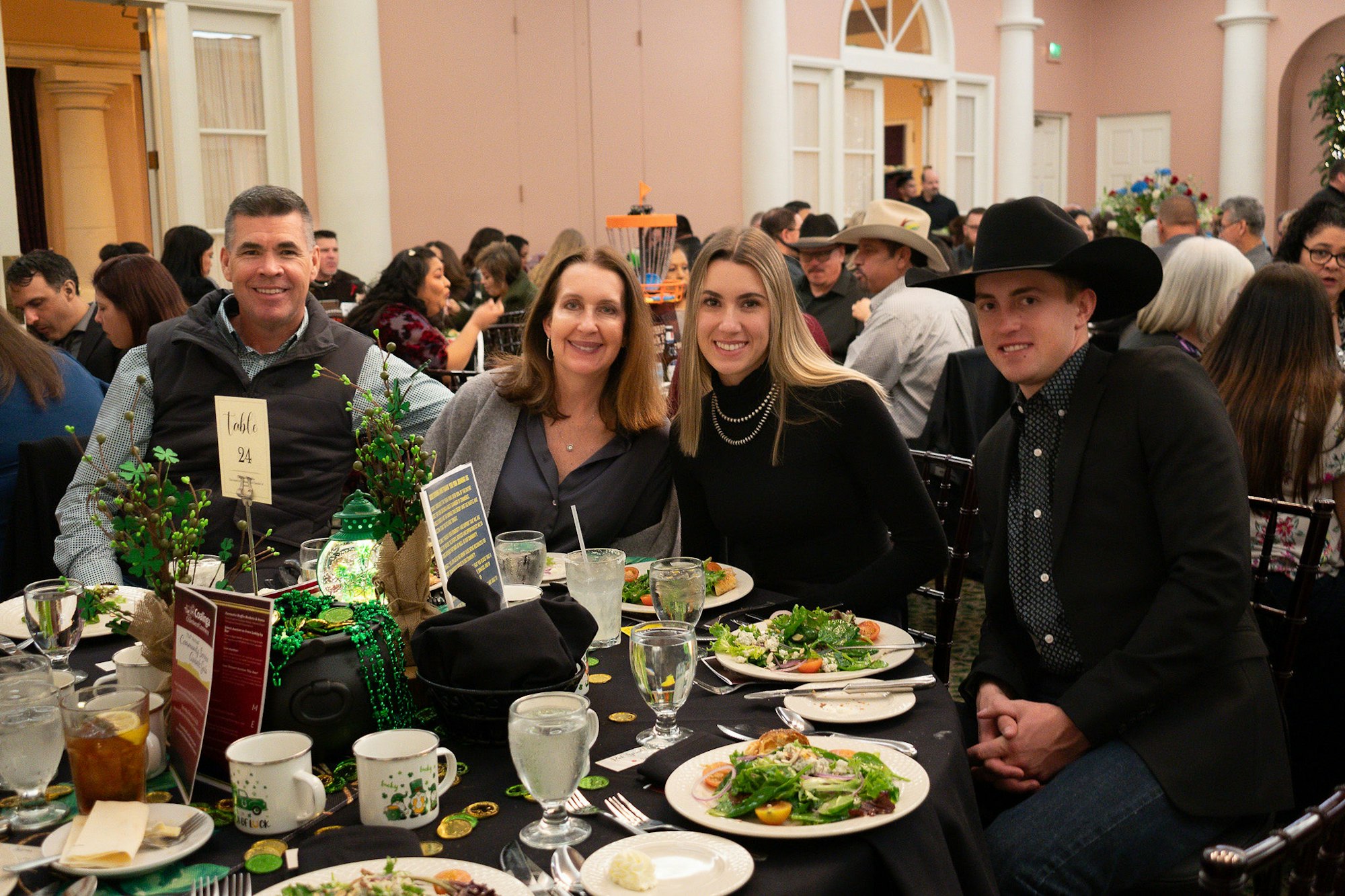 Four people posing at a decorated table with meals, at an indoor event, smiling for the camera.