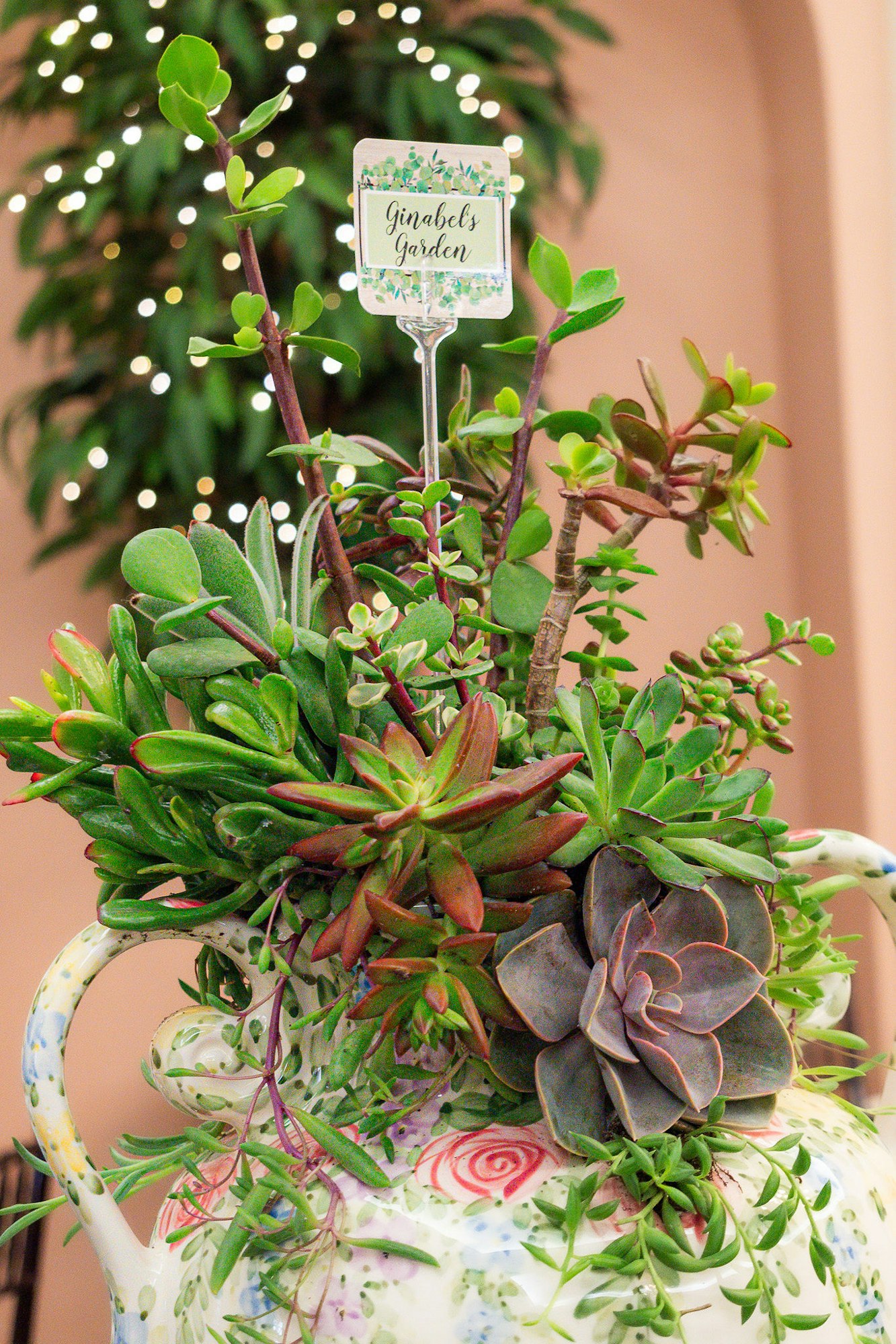 A teapot turned into a succulent planter with a sign reading "Ginabel's Garden."