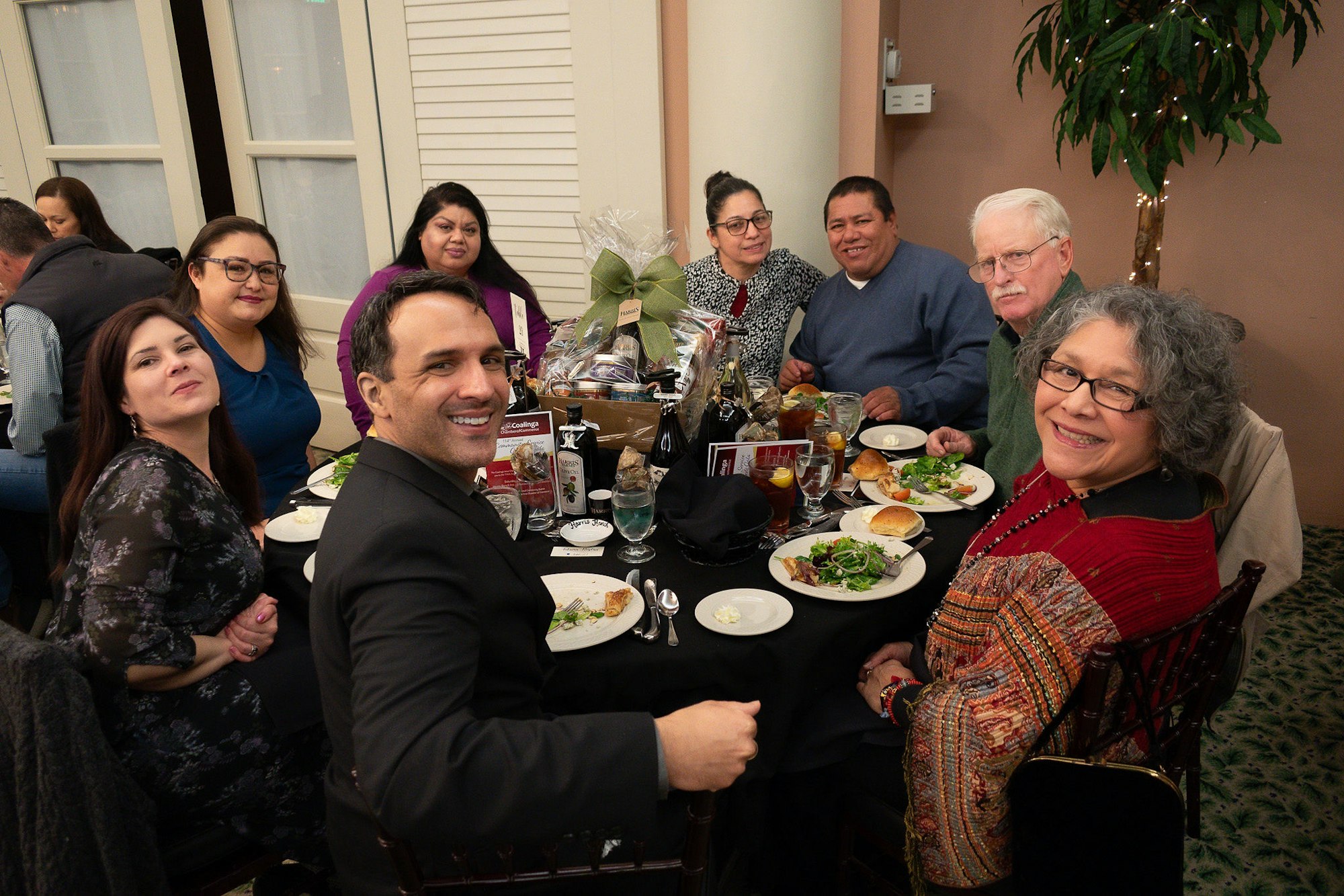 Group of people enjoying a meal together at a table with a gift basket centerpiece.