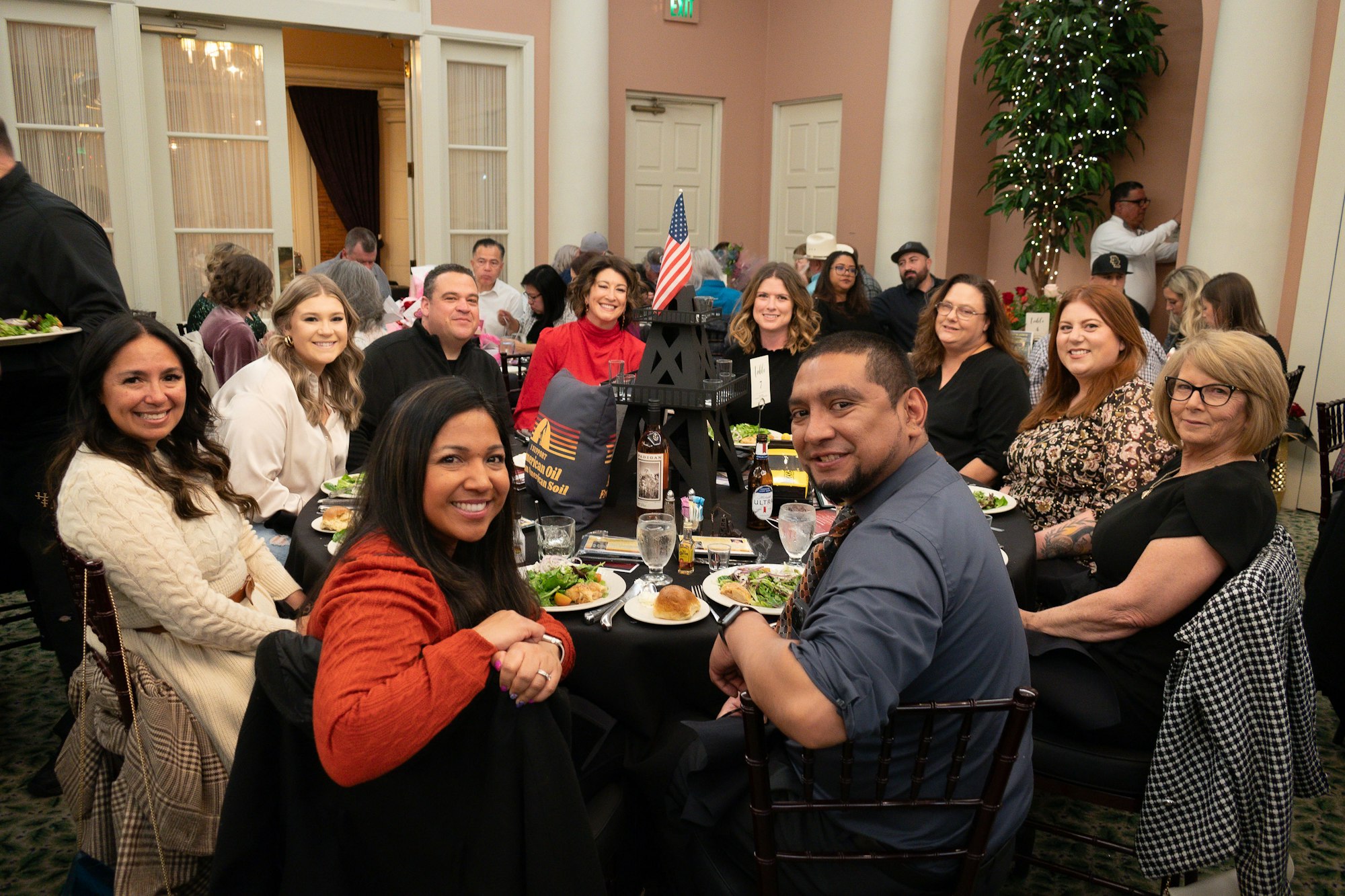 Group of people smiling around a dinner table at a formal event with an American flag centerpiece.