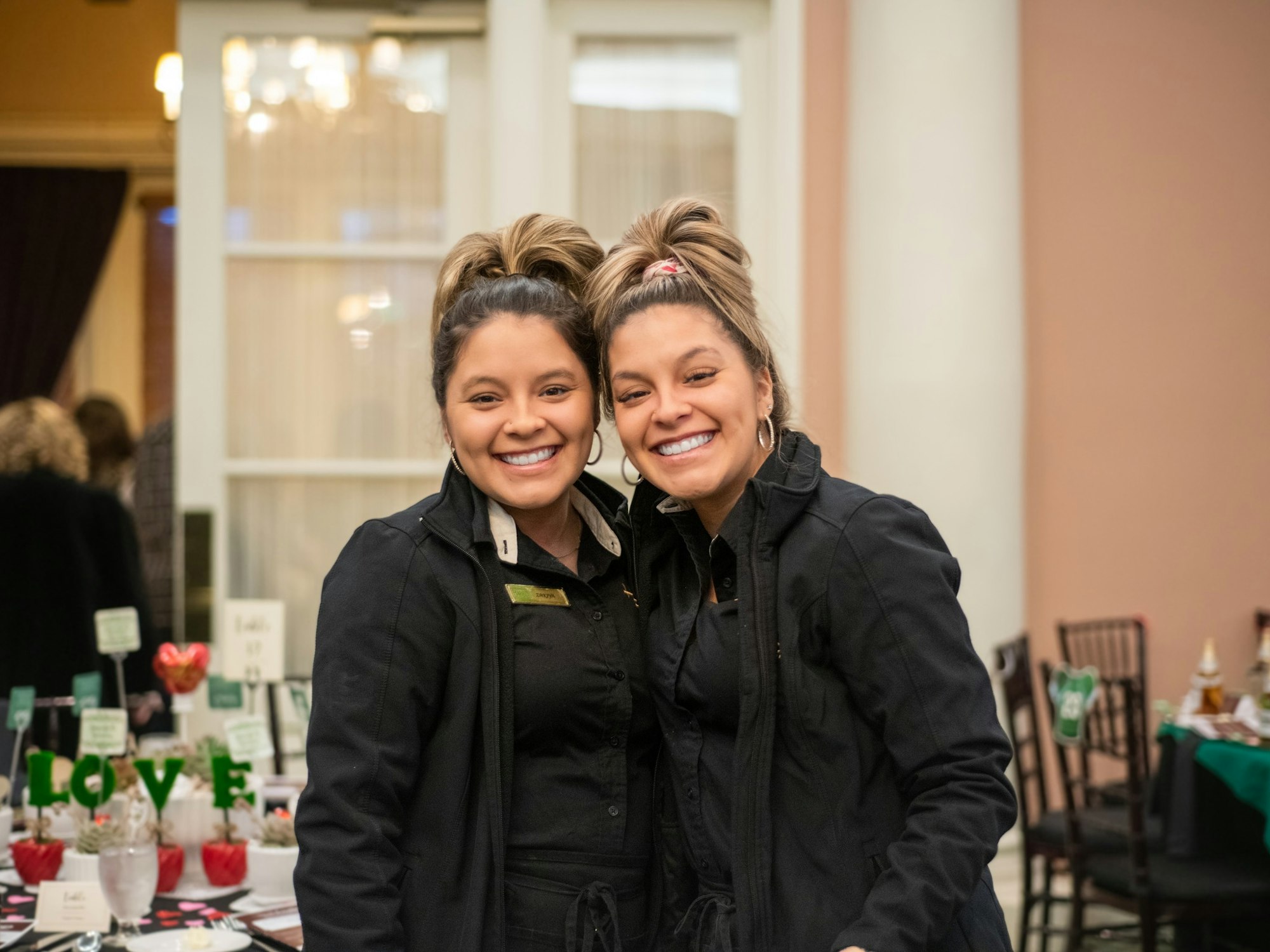 May contain: clothing, coat, jacket, face, head, person, photography, portrait, dining table, furniture, table, architecture, building, dining room, indoors, room, happy, smile, adult, female, woman, and restaurant