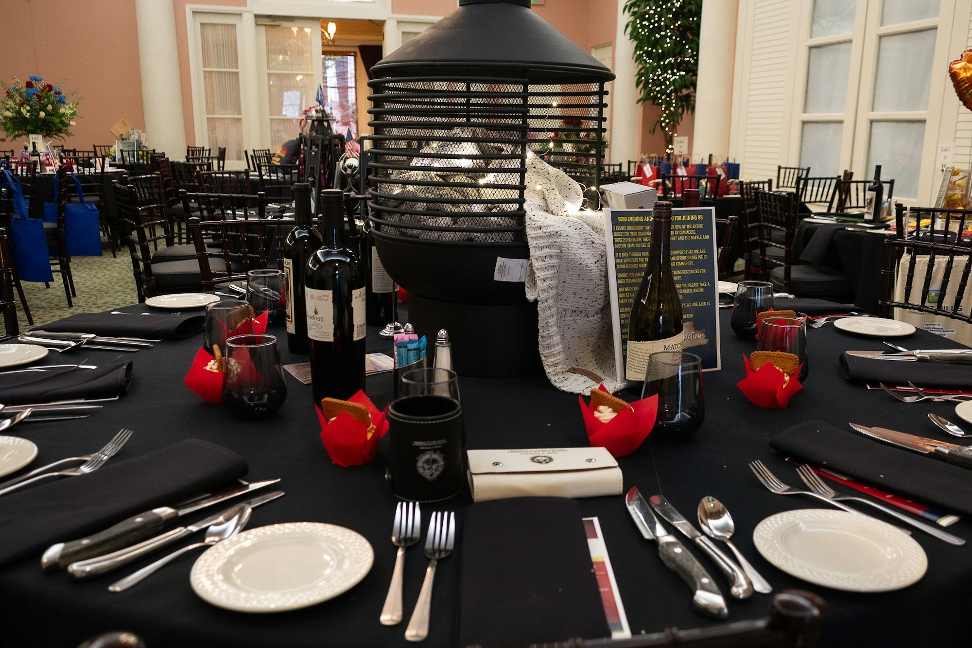 Banquet setup with black tablecloths, wine bottles, glasses, and a large decorative grill centerpiece.