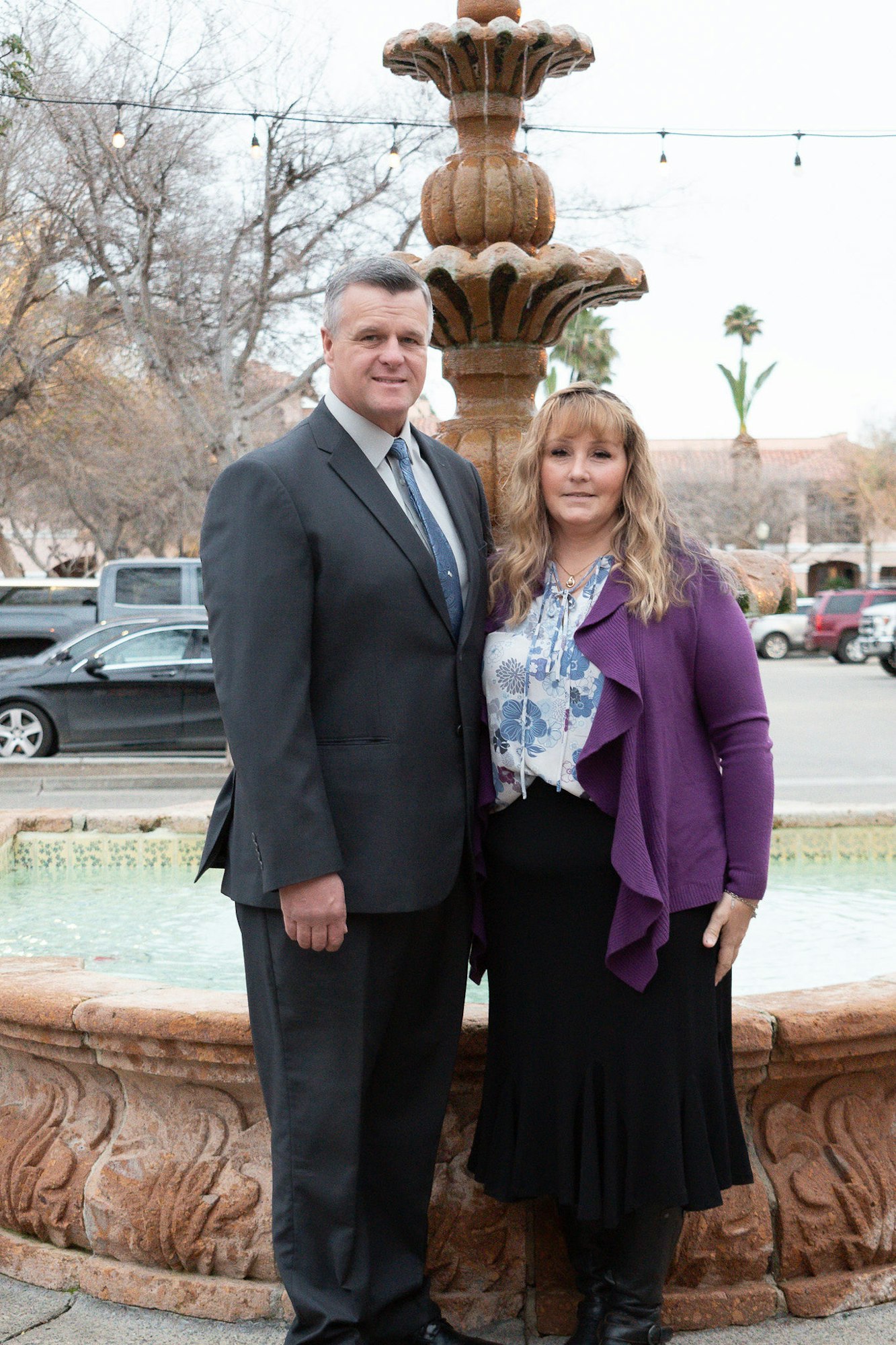 Two people standing by a fountain with string lights and trees in the background.