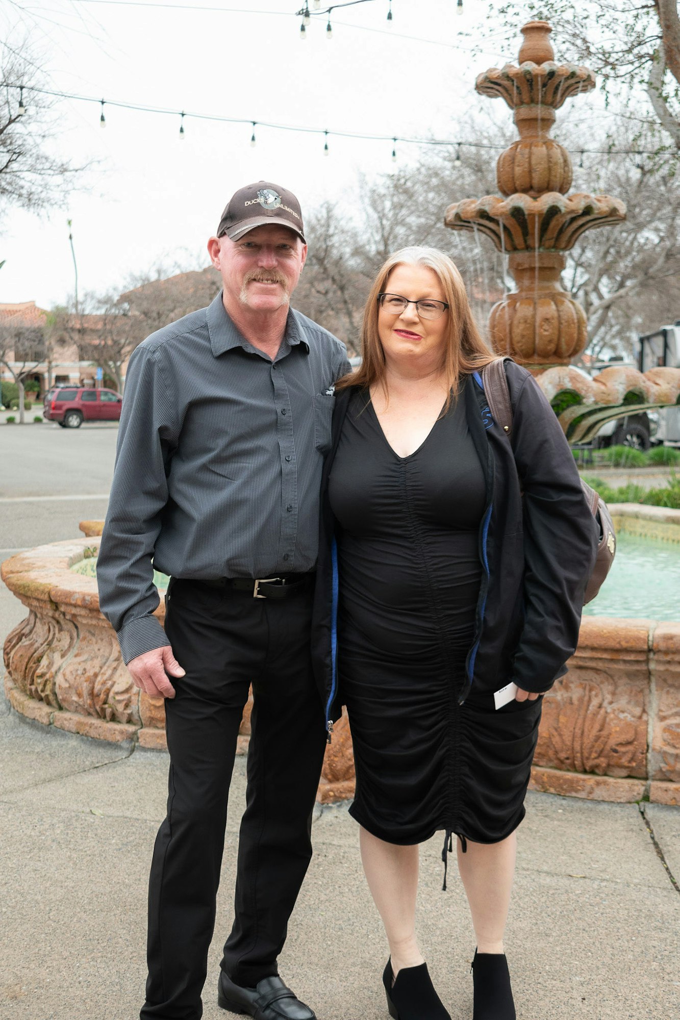 A man and a woman standing in front of a fountain with string lights above.