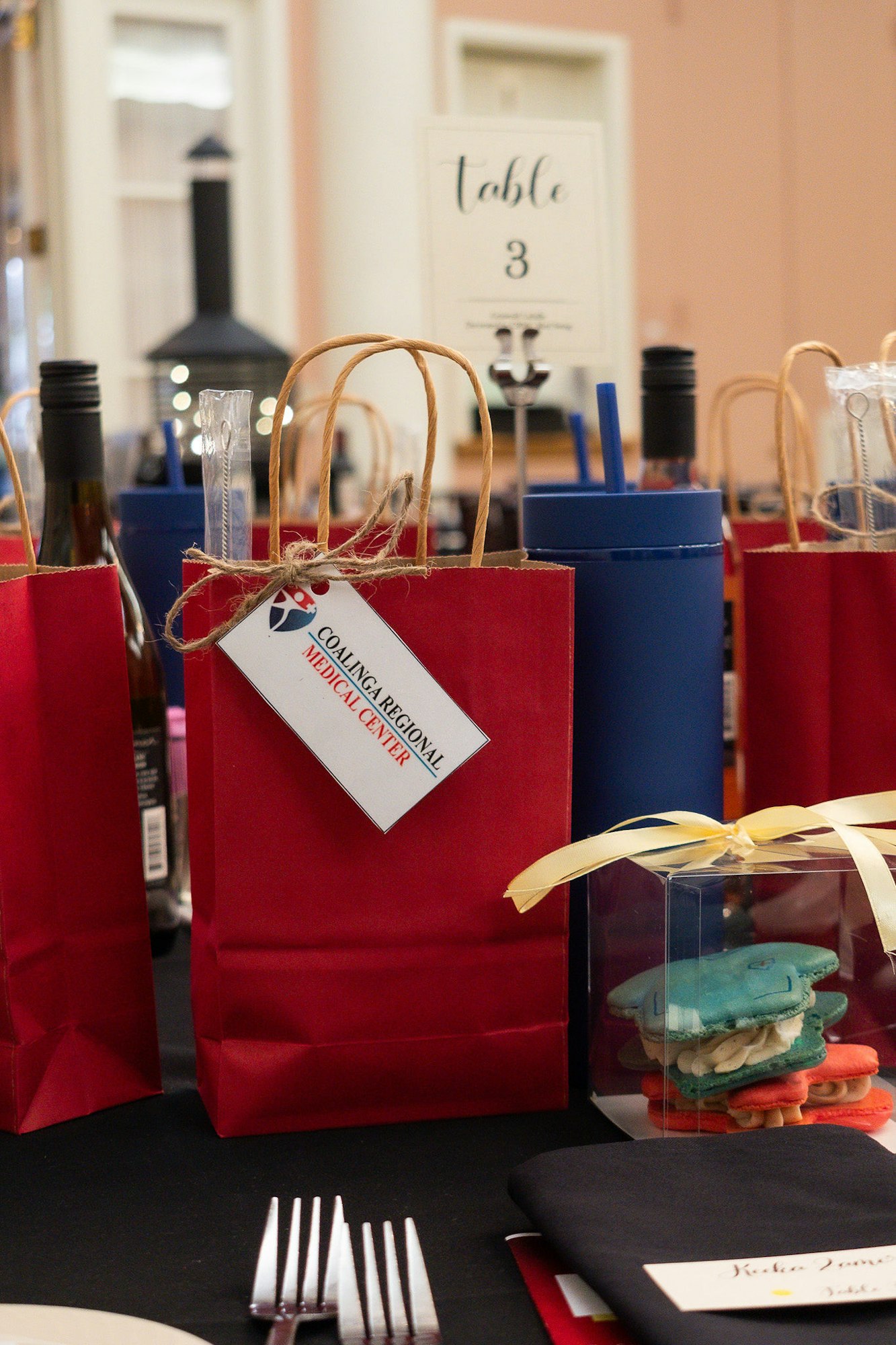 An event table setting with gift bags, wine, a table number sign, and boxed macarons.
