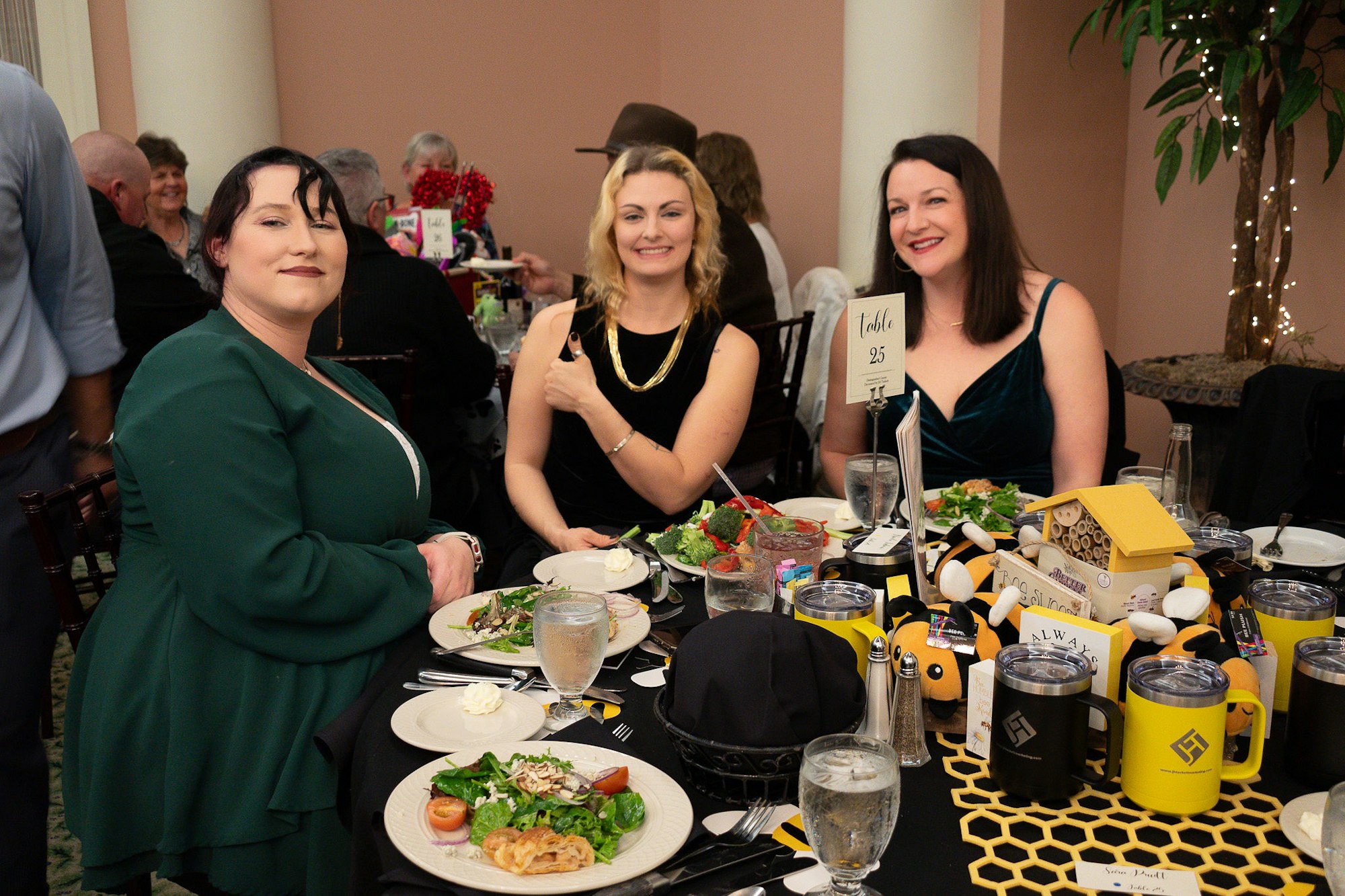 Three people at table 25 with dinner plates, drinks and a bee-themed centerpiece.