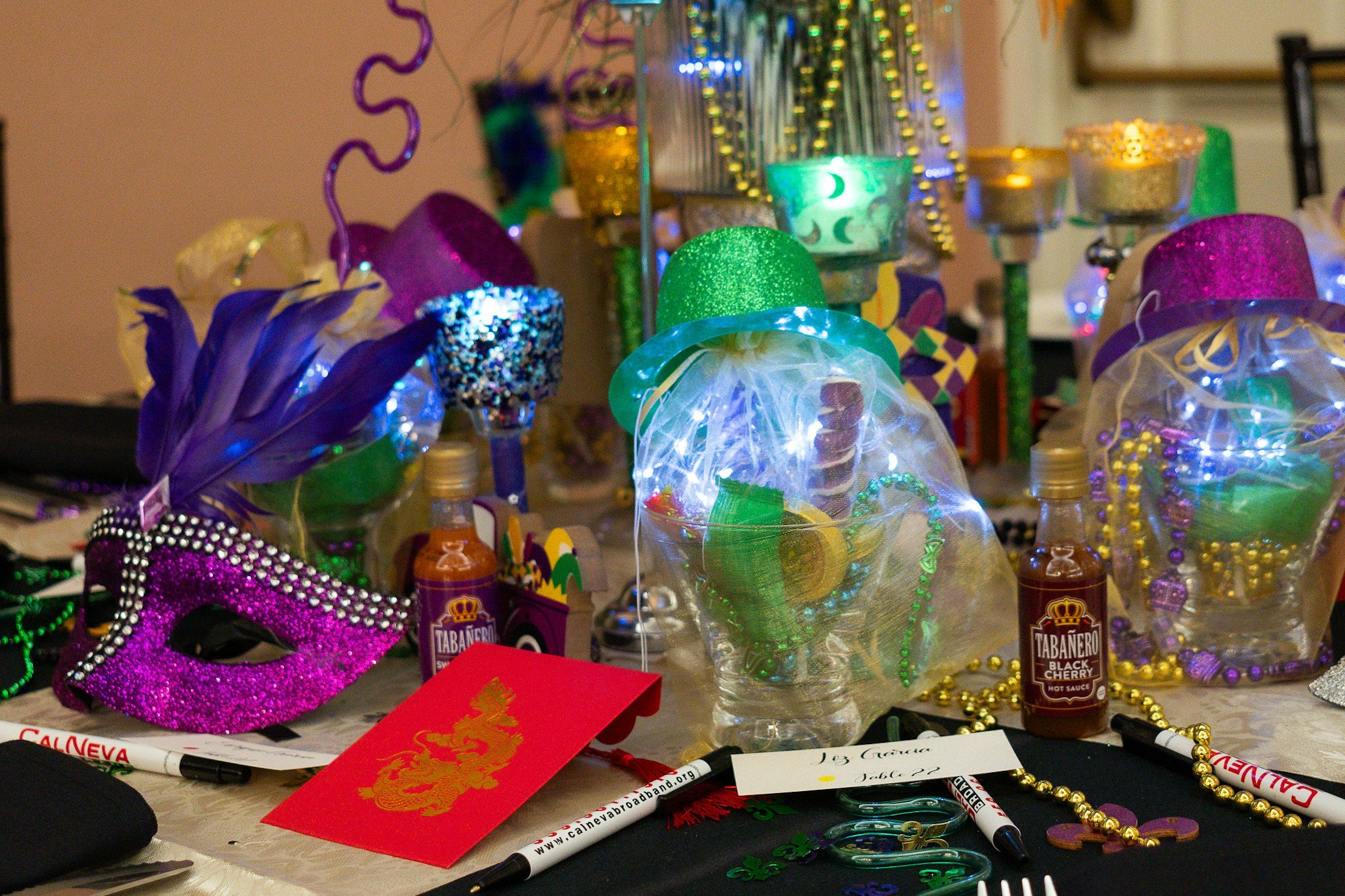 A vibrant Mardi Gras table setting with masks, beads, hats, and decorative cups.
