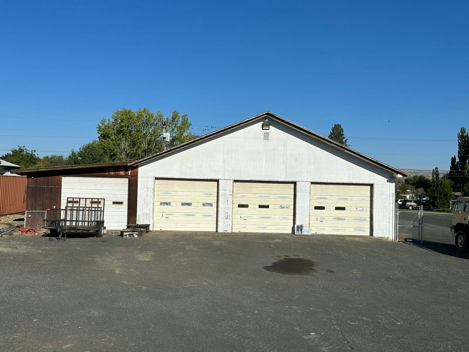 The image features a garage with three large doors, a clear blue sky, and some surrounding vegetation.
