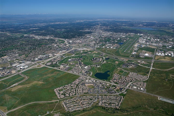 Aerial view of a Meridian with residential areas, roads, a golf course, and a small body of water. Mountains in the distance.