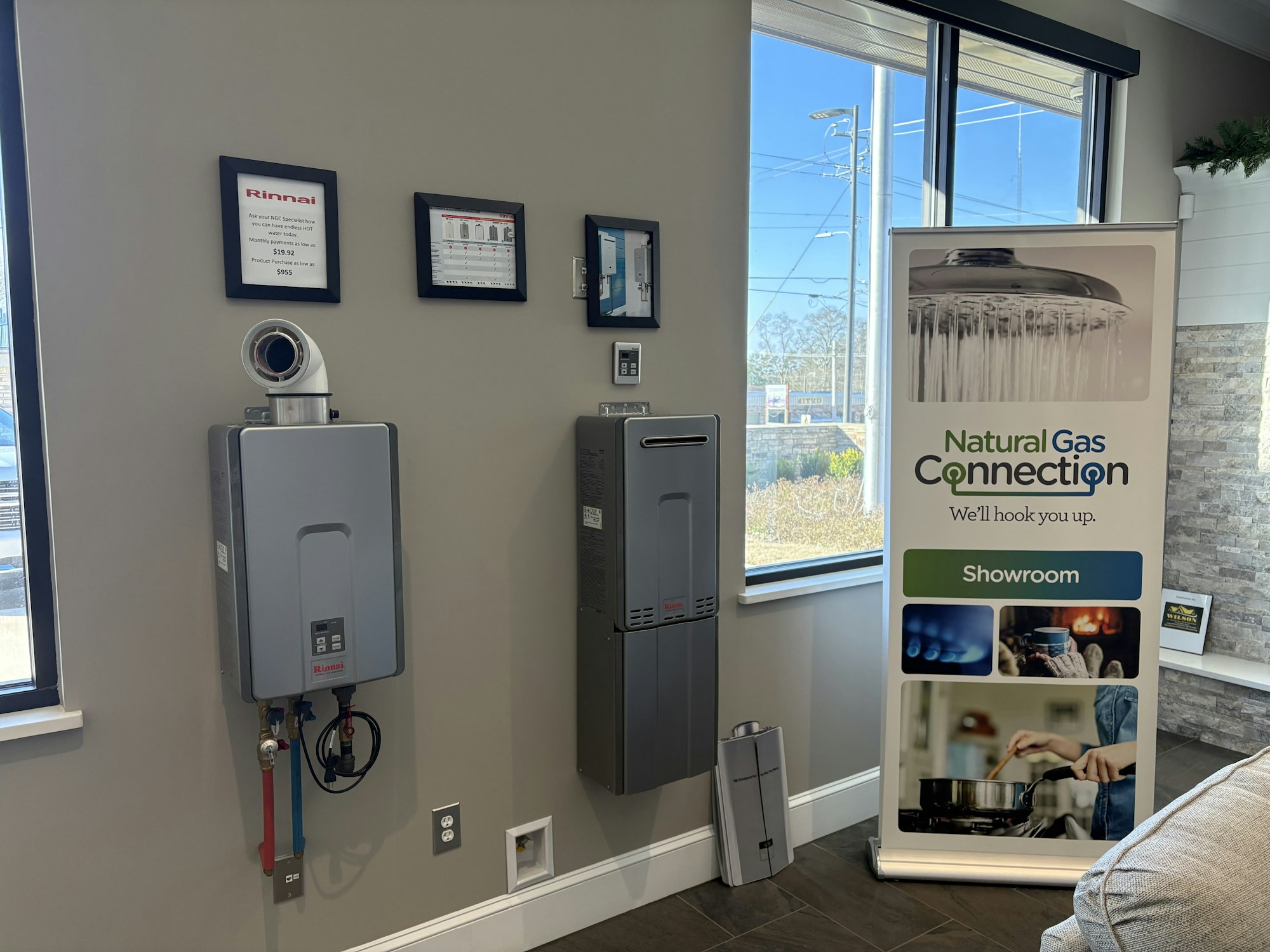 The image shows a showroom with a Rinnai water heater, informational signs, and a display banner for natural gas connections.