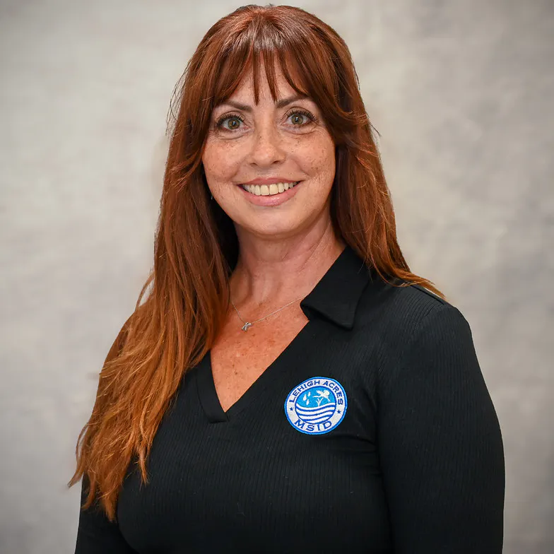 A woman with long red hair is smiling at the camera, wearing a black shirt with a LAMSID logo. Background is neutral.