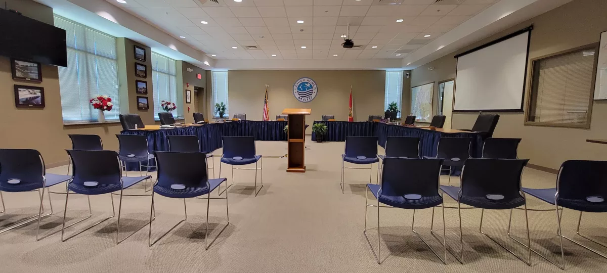 Empty meeting room with chairs, a podium, flags, and a projection screen.