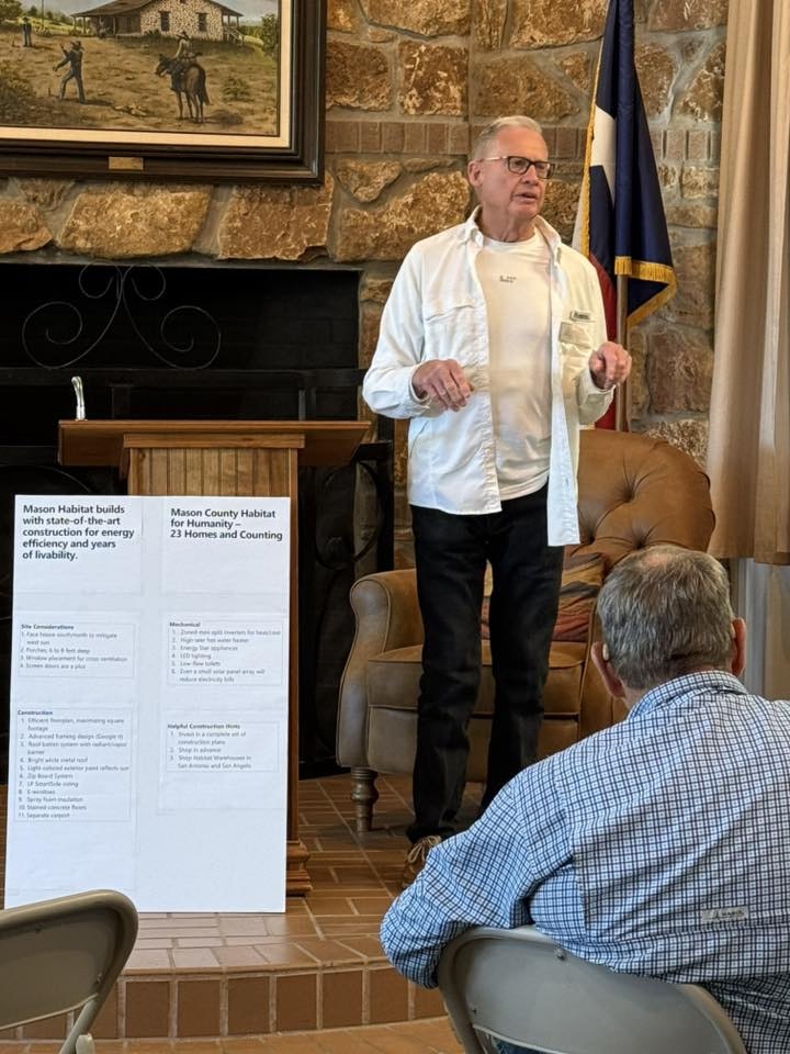 A speaker discusses Mason County Habitat for Humanity, highlighting their construction methods and achievements, with an audience present.