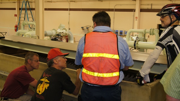 Four people in a workshop, one wearing a safety vest, discussing machinery or equipment.