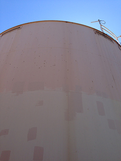 A large cylindrical tank with patches and a blue sky background.