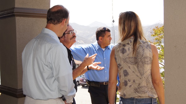 Four people standing outside, engaged in conversation near a building, with a mountainous landscape in the background.