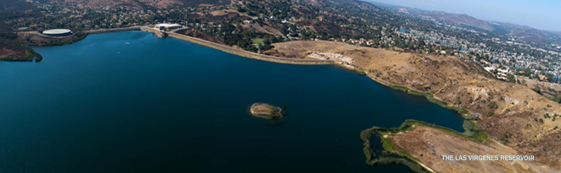Aerial view of Las Virgenes Reservoir, surrounded by hills and a developed area in the background.