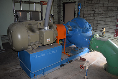 Industrial machinery with a large motor and piping system, possibly a pump, set on a blue base indoors.