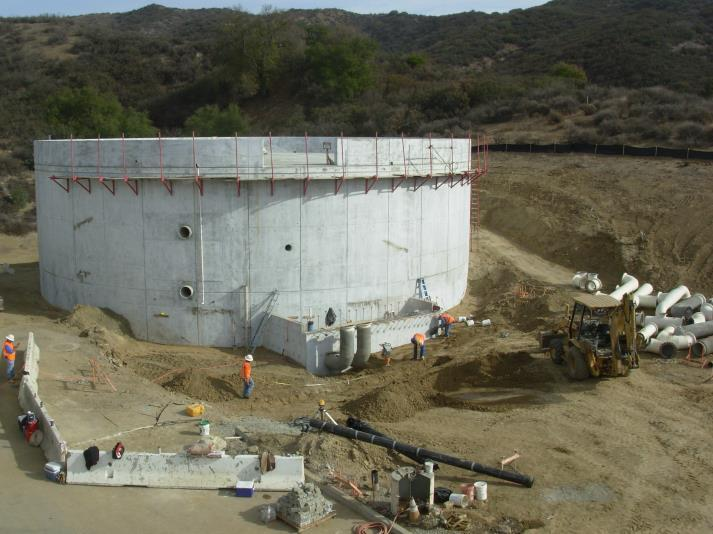 Construction site with a large circular concrete structure, workers, and a bulldozer.