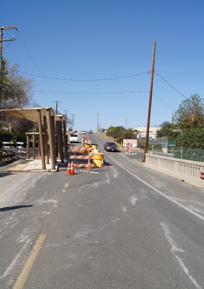 Road under construction with barriers, cones, and vehicles moving through.