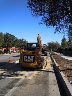 Construction equipment with "CAT" logo on a roadside, surrounded by trees and traffic cones under a clear blue sky.