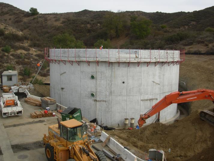 Large concrete tank under construction with heavy machinery and workers around it.