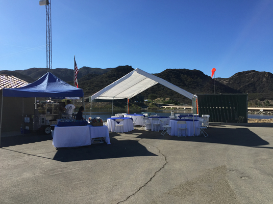 Outdoor setup with tents, tables, and chairs, against a mountainous backdrop under a clear sky.