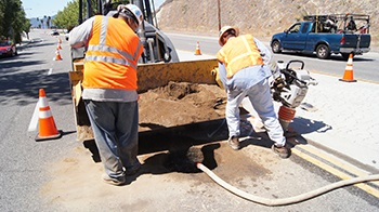 Construction workers in safety vests doing road work with cones and equipment on a sunny day.