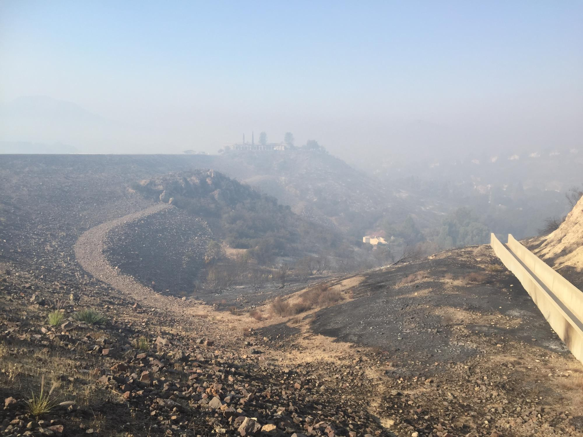 Hazy landscape with a rocky path and burnt terrain. Buildings appear faintly in the background.