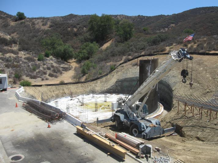 Construction site with a crane, concrete foundation, and American flag in a hilly landscape.
