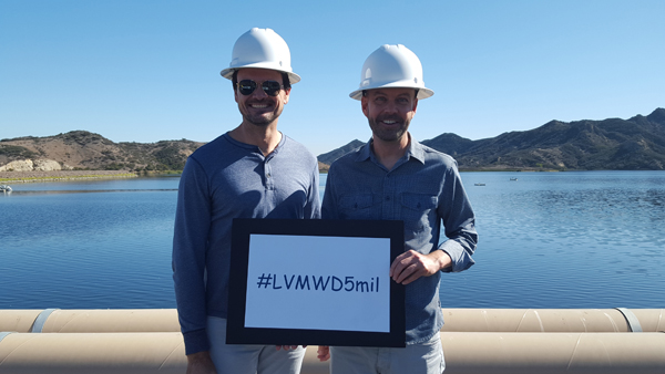 Two people in hard hats by a lake, holding a sign with "#LVMWD5mil."
