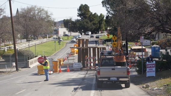 Road construction site with barriers, cones, a "Road Closed" sign, and workers; a truck is parked nearby.