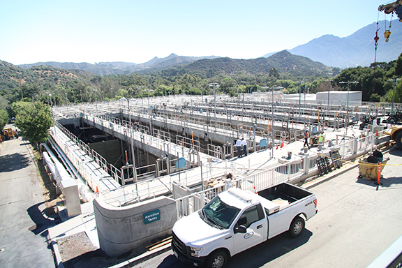 A water treatment facility with multiple tanks, surrounded by hills, and a parked pickup truck in the foreground.