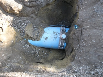 A large blue pipe partially buried in the ground, surrounded by dirt and rocks.