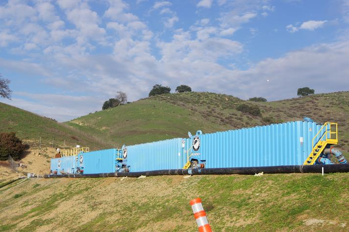 Three large blue containers on a hillside with a cloudy sky above.