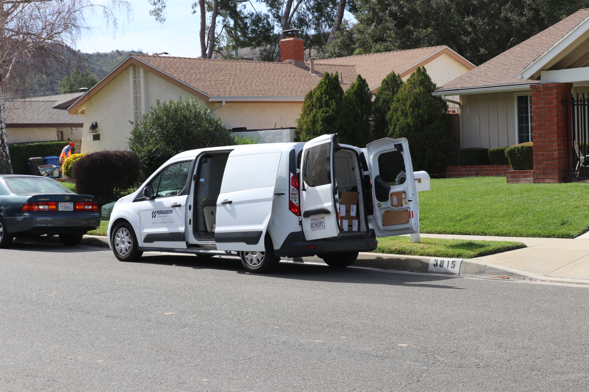 A white delivery van with open doors is parked on a residential street.