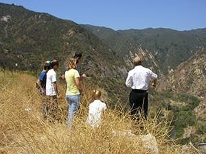 A group of people stand on a grassy hill overlooking a mountainous landscape.