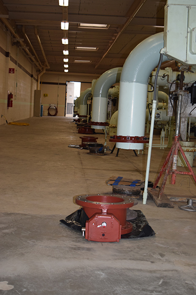 A large industrial room with pipes, ducts, and equipment, including a red valve in the foreground.