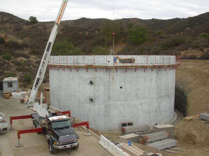 Construction site with a large circular concrete structure, crane, and truck surrounded by hills.